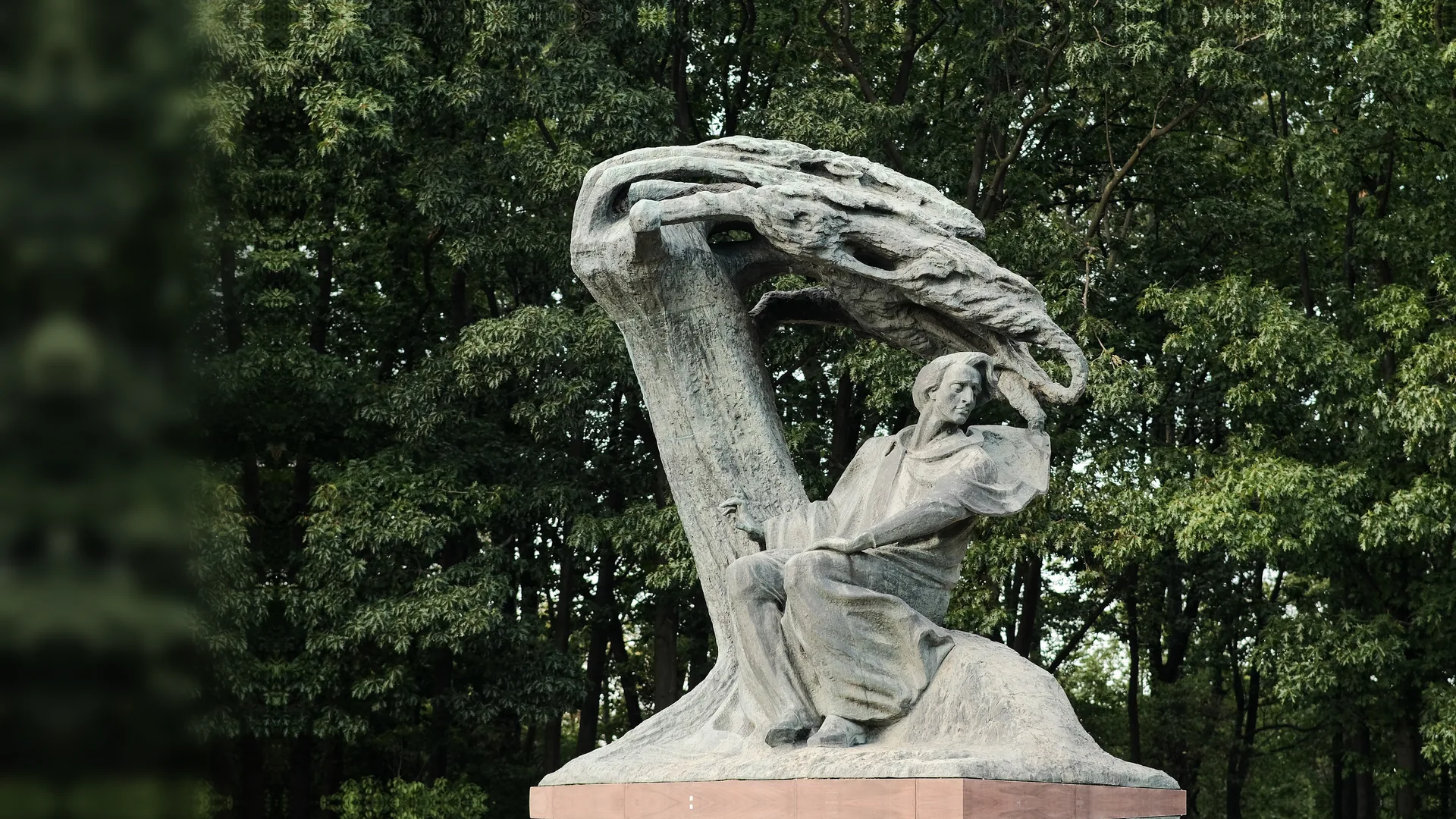 Бронзовий пам'ятник Шопену в варшавському парку Лазенки: композитор сидить під широкою металевою кроною у формі верби, позаду — зелені дерева.